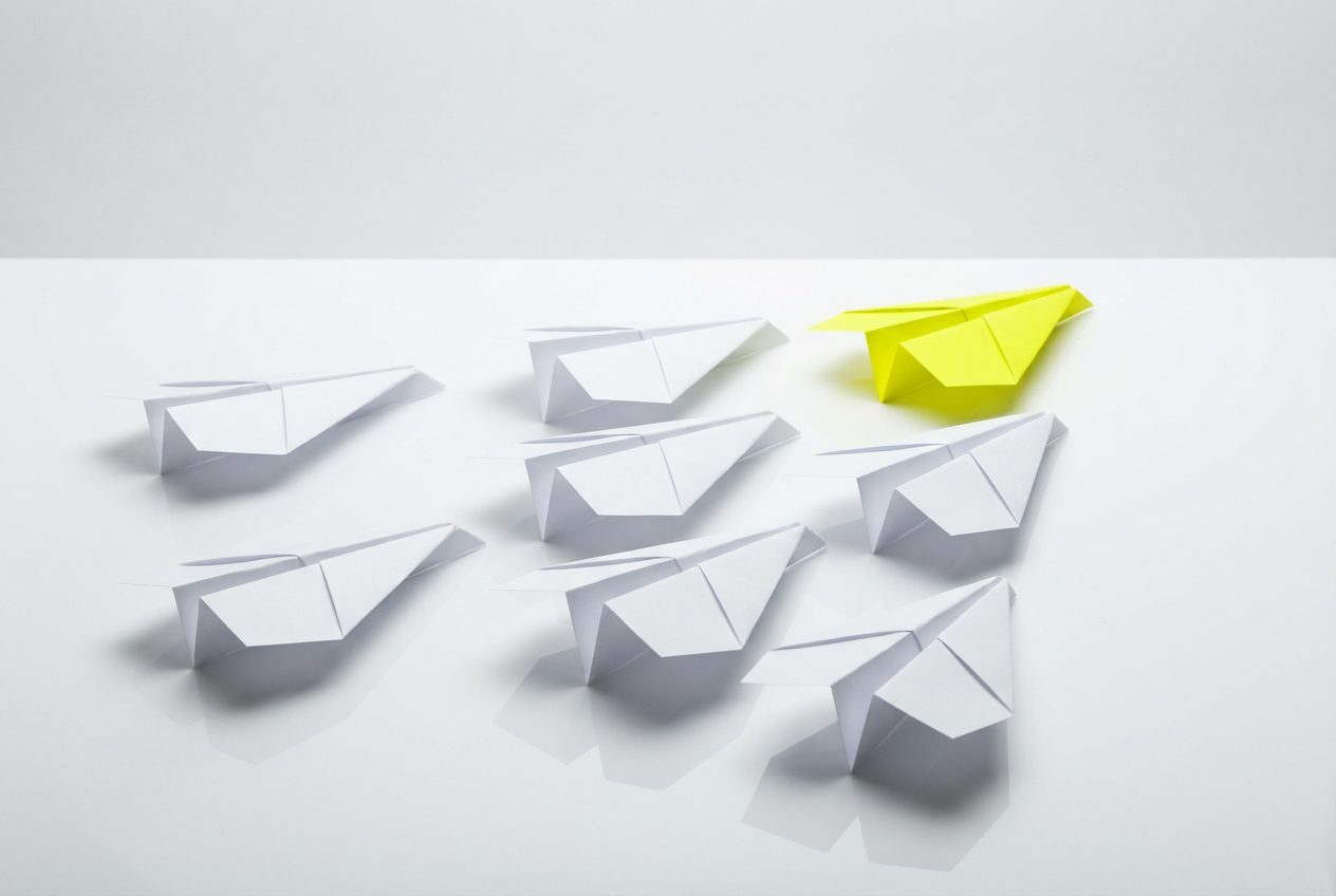 White paper aeroplanes with one yellow plane leading.